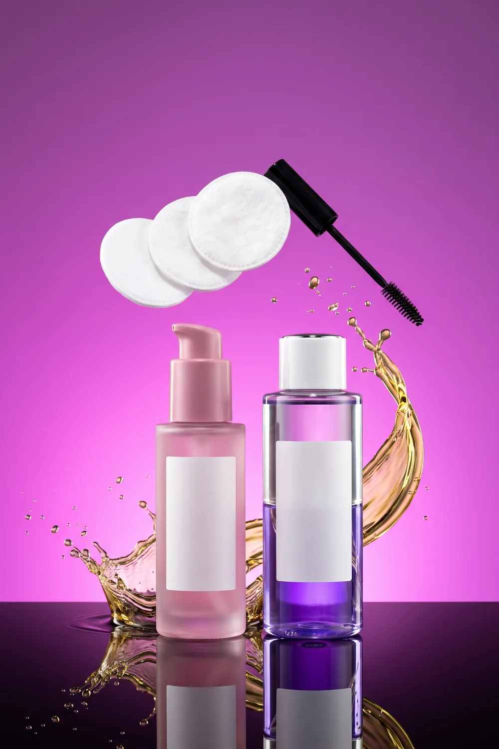 Unbranded eye makeup remover bottles in colored glass on a cobalt and aqua backdrop, with a two-layer blue and clear liquid, cotton pads and droplets in mid-air