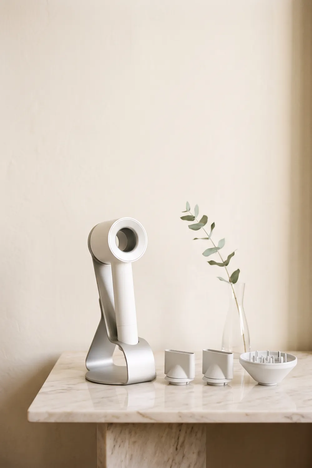 An unbranded fuchsia and gray ring-headed hair dryer resting on cream linen on a pale marble vanity, beside its magnetic attachments, a round brush and a silk scrunchie in morning window light